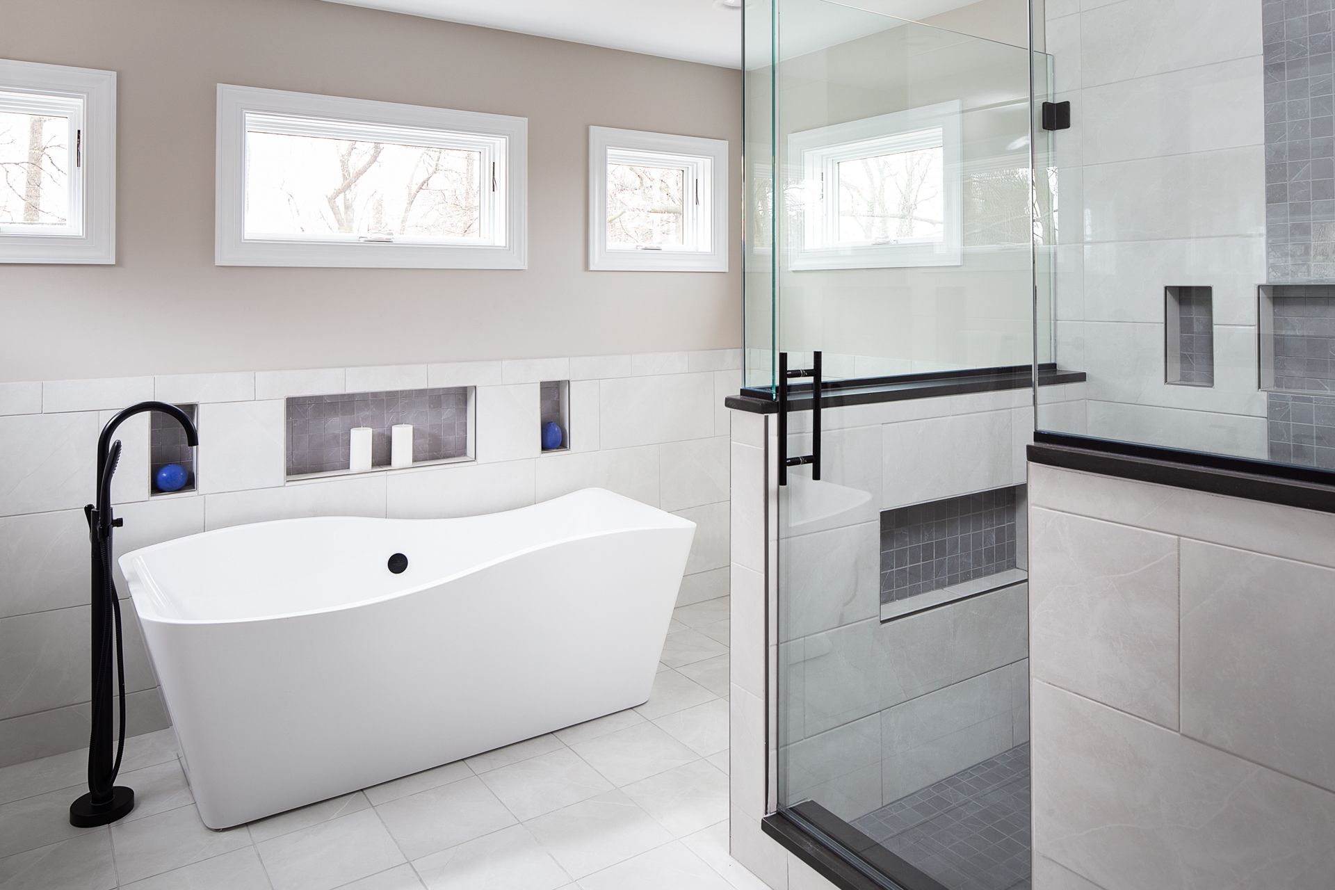 Modern, renovated bathroom with white tile, standalone tub, and separate glass-enclosed shower. 