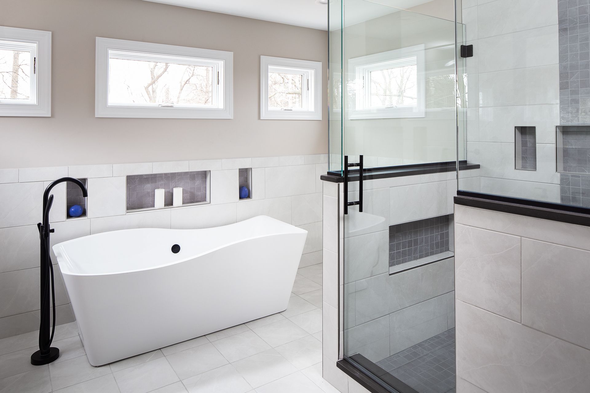 Modern, renovated bathroom with white tile, standalone tub, and separate glass-enclosed shower.