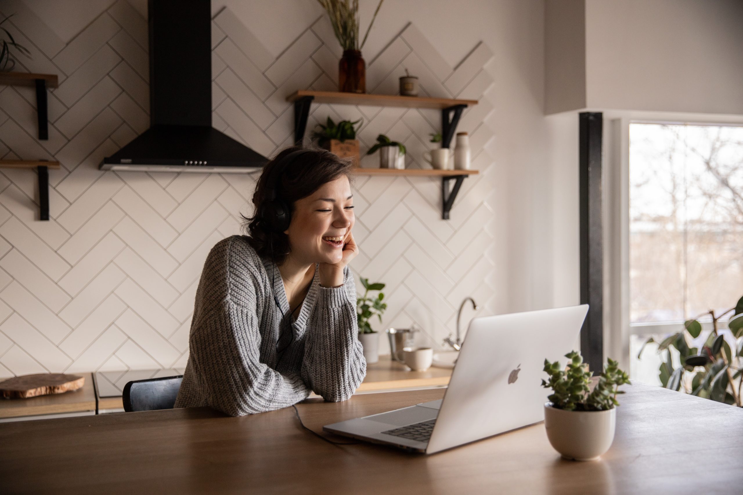 Woman working on laptop and smiling in kitchen.