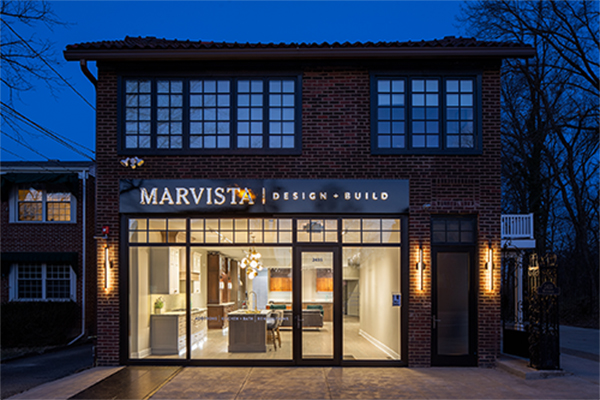 Marvista showroom with lights on in small brick building at dusk.