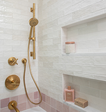 Remodeled shower with white subway tile, accent line of pink tiles just above tub, and brushed gold fixtures.