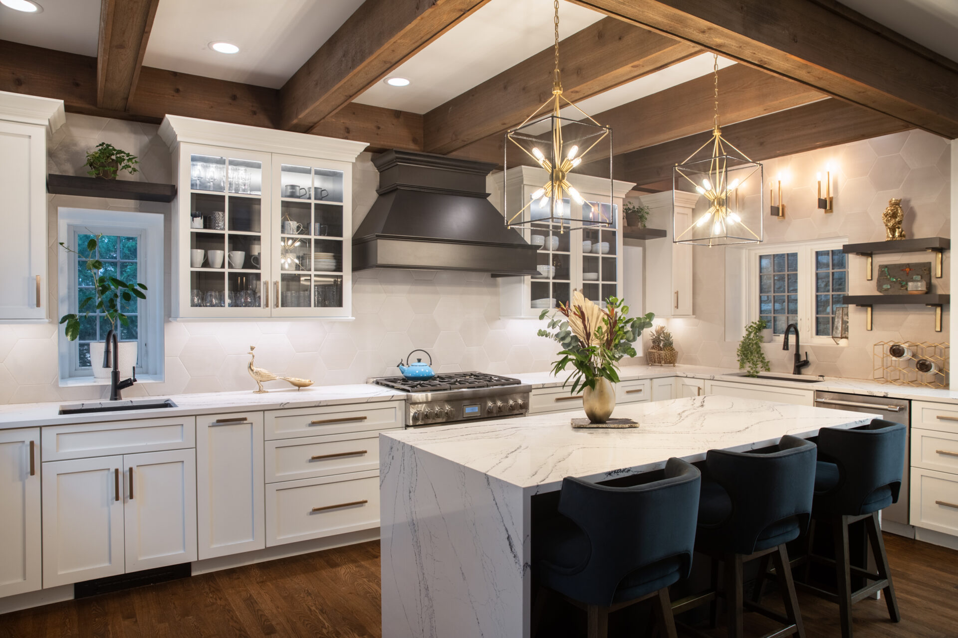 Remodeled kitchen with wood beams on ceiling, white cabinets and white marble countertops with waterfall edge on island, with row of three seats.
