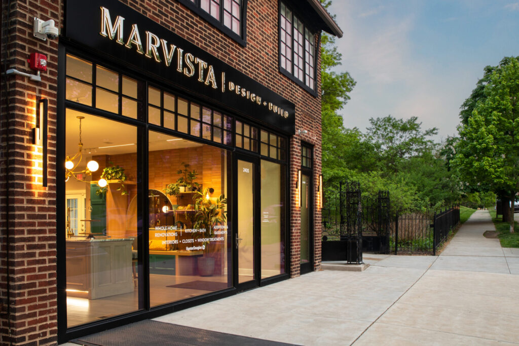 Front of Marvista Design + Build showroom. Brick building with large glass windows and lights on inside.